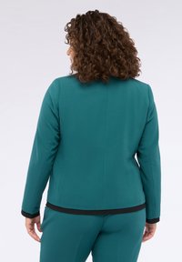 Blazer teal con una vestibilità su misura, maniche lunghe e dettagli neri all'orlo. Tessuto liscio, design strutturato, vista posteriore mostrata.