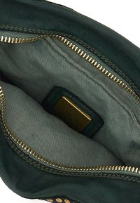 Interno di una borsa verde in pelle che mostra una cerniera dorata, fodera grigia e un'etichetta del produttore. La cerniera presenta un design distintivo con denti metallici.