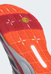 Schoenzool met een gestructureerd oranje en rode rubberen ontwerp, voorzien van een cirkelvormige gele accent en een witte sleuf aan de zijkant.