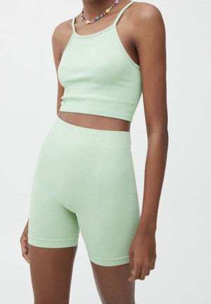 Vrouw draagt een lichtgroene geribbelde cropped top met spaghettibandjes en bijpassende hoogwater geribbelde biker shorts.