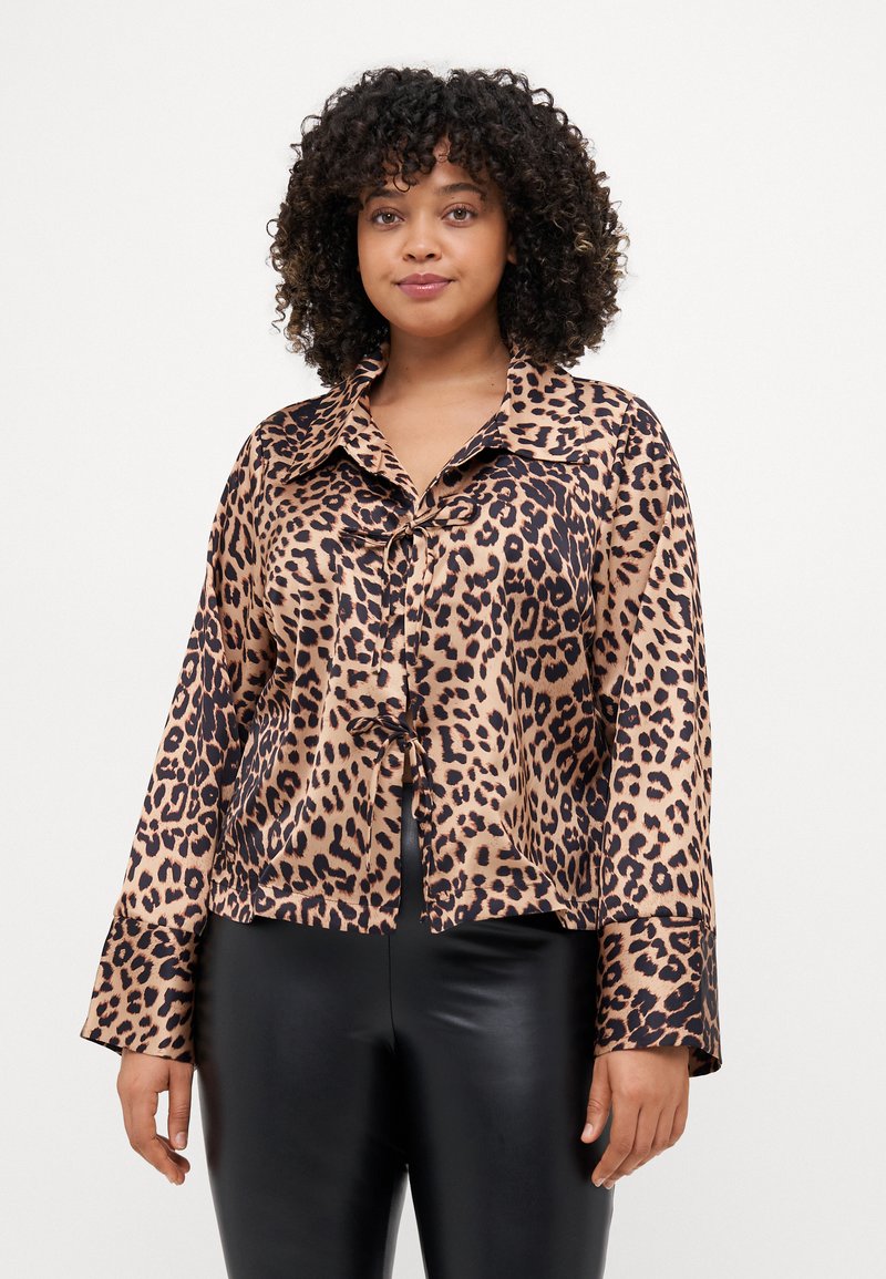 Blusa em tecido satinado com padrão de leopardo, apresentando um fecho frontal com botões, colarinho largo, mangas longas e um design cropped. Acabamento texturizado e suave.