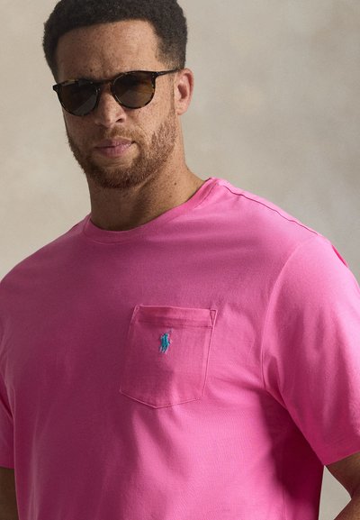 Ροζ βαμβακερό μπλουζάκι με κοντά μανίκια, με τσέπη στο μπροστινό μέρος και μικρό μπλε κεντητό λογότυπο. Λείο ύφασμα, άνετη εφαρμογή.