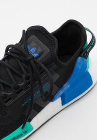 Svart stickad Adidas-sneaker med svarta snören, blå och teal-accenter, vit sula och med en märkeskappa på hälen.