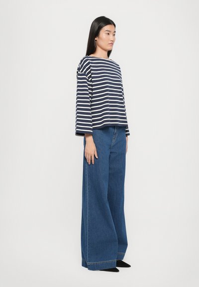 Striped navy and white long-sleeve top paired with high-waisted wide-leg denim jeans. The outfit has a relaxed fit and a casual design.