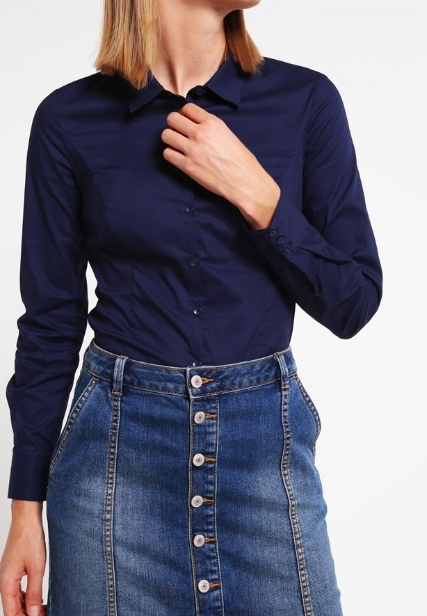 Chemise bleu marine à manches longues avec un design à boutons, associée à une jupe en denim avec une fermeture à boutons sur le devant et des poches.