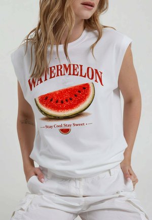 Donna con maglietta bianca senza maniche con grande grafica di una fetta di anguria e testo "Watermelon Stay Cool Stay Sweet" sul davanti.