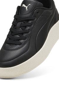 Czarne skórzane sneakersy Puma z czarnymi sznurowadłami i białą gumową podeszwą, ukazujące teksturowany uchwyt i logo Puma na języku.
