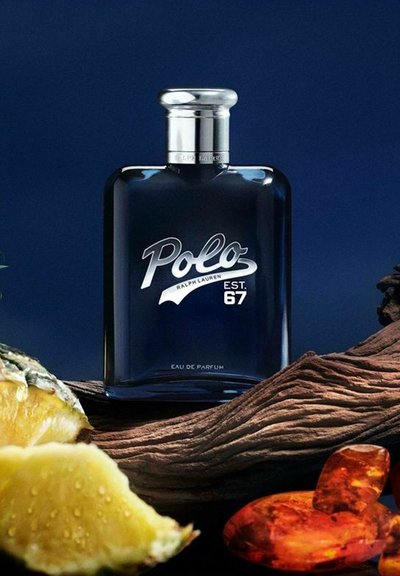 En mörk glasparfymflaska märkt "Polo" omges av skivor av ananas och träbitar, med en rik blå bakgrund.