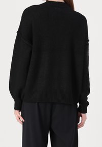 Schwarzer Strickpullover mit lockerer Passform, rundem Ausschnitt und geripptem Saum. Verfügt über überschnittene Schultern und ein strukturiertes Material für zusätzlichen Tiefeneffekt.
