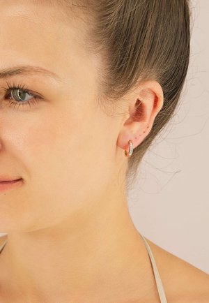 Roségoldene Creolen mit einem funkelnden, diamantenähnlichen Akzent, glatter Oberfläche und kreisförmiger Form, die am Ohr getragen werden.