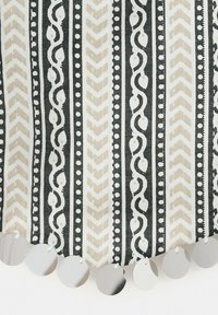 Tissu rayé vertical noir et beige avec motifs abstraits et disques métalliques ronds argentés suspendus le long du bord.