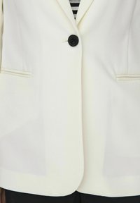 Hvid blazer med en enkelt sort knap, slagkraver og sidelommer. Glat tekstur med en struktureret pasform.