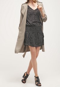 Šaty s černobílým vzorem a rozšířenou sukní, vrstvené pod světle šedým trenčkotem. V doplnění s černými sandály s pásky.