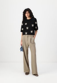 Top corto nero a maniche corte con ricami floreali, pantaloni beige a gamba larga e scarpe con stampa leopardata. Tiene una piccola borsa a tracolla blu.