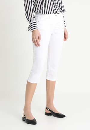 Valkoiset capri-housut, jotka on valmistettu kevyestä kankaasta, ja joissa on slim fit -malli ja sivurei'ät. Yhdistetty mustiin kärkitossuihin.