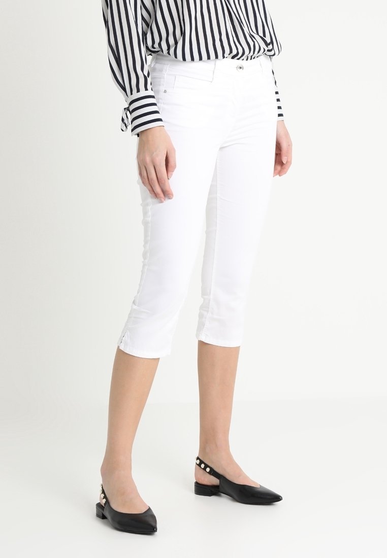 White capri pants made from lightweight fabric, featuring a slim fit and side slit details. Paired with black pointed-toe flats.