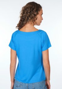 Blaues T-Shirt mit kurzen Ärmeln und weitem Ausschnitt, aus glattem Material, mit einer lockeren Passform und Raglan-Ärmeln, kombiniert mit Jeans-Shorts.