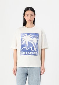 Camiseta de gran tamaño color crema con un gráfico azul que presenta palmeras y un sol, y el texto "BILLABONG" en letras blancas en bloque.