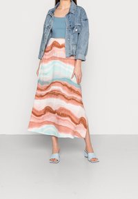 Vaaleansininen cropped-top, farkkutakki ja pitkä hame, jossa on aaltoilevia kuvioita persikassa, vaaleanpunaisessa, vaaleansinisessä ja pronssinvärisissä aksenteissa. Vaaleansiniset sandaalit.