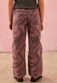 Weiß- und schwarze Zebraprint-Hosen im weiten Schnitt mit zwei Gesäßtaschen und einem ausgefransten Saum, kombiniert mit schwarzen Slippern.