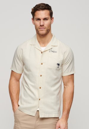 Camicia a maniche corte di colore crema con bottoni marroni, "Venezia" ricamato e un design di palma sulla tasca del petto. Tessuto leggero.
