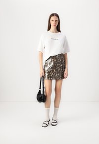 Witte relaxte T-shirt met tekst, glanzende luipaardprint mini-rok, witte kniehoogsokken, zwarte sandaal en een zwarte handtas.