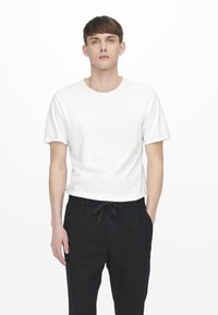 Witte katoenen t-shirt met ronde hals en korte mouwen, gecombineerd met zwarte broek met trekkoord. Eenvoudig, onopgesmukt ontwerp.