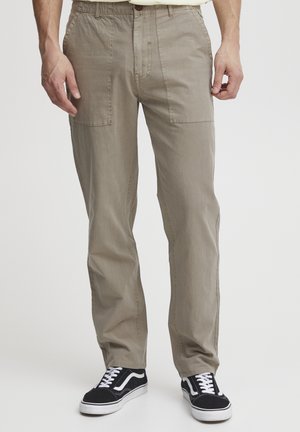 Beige cargo pants with a button closure, two front pockets, and a comfortable fit. Worn with black sneakers featuring white accents.