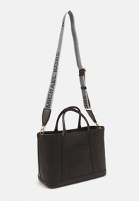 Sac fourre-tout en cuir noir avec une surface texturée, des poignées supérieures doubles et une bandoulière grise amovible avec l'inscription "Michael Kors". Accents en matériel doré.