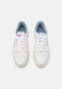 Białe skórzane sneakersy z jasnoniebieskimi akcentami, okrągłym noskiem, perforowanymi detalami, płaskimi białymi sznurowadłami i beżową gumową podeszwą. Marka Reebok na języku.