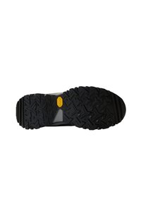 Svart gummi yttersåle på en sko med dype, vinklete dekkmønstre og en gul Vibram-logo i midten.