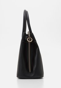 Svart läderhandväska med en slät textur, hög form och en gyllene rund hårdvaruaccents. Har två långa handtag och en dragkedjestängning.