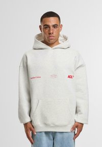 Šedá bavlněná mikina s kapucí a přední kapsou, s červeným výšivkou "Another Cotton" a "ACL." Volný střih a velká, pohodlná kapuce.