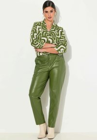 Zielona, wzorzysta bluzka z rękawami do połowy przedramienia, zestawiona z dopasowanymi zielonymi spodniami z imitacji skóry oraz beżowymi botkami za kostkę.