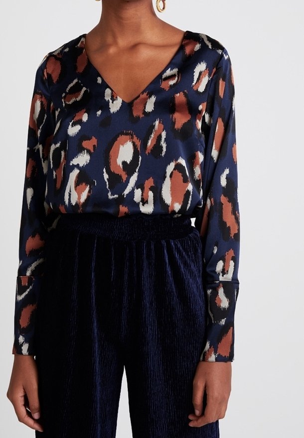 Marinblus med v-ringning och långa ärmar, prydd med ett leopardsmönster i bruna, vita och rostfärgade nyanser. Texturerad tyg och avslappnad passform.