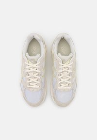 Chaussures de course légères en mesh blanc et beige, avec des accents jaune clair, dotées d'un bout arrondi, d'une languette rembourrée et de lacets plats.