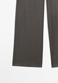 Pantaloni a gamba larga grigio scuro con motivo a righe sottili, caratterizzati da una texture liscia e una finitura su misura, che mostrano un orlo pulito nella parte inferiore.