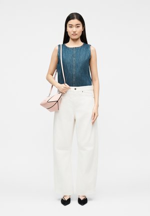 Γυναίκα με αμάνικο τοπ από τζιν, λευκό παντελόνι φαρδιάς γραμμής, μαύρα μυτερά παπούτσια και κρατώντας μια ροζ γεωμετρική τσάντα χιαστί.