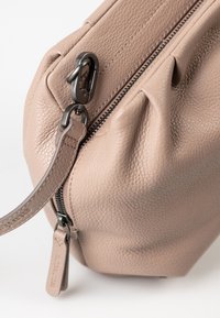 Tasche aus braunem Leder mit strukturiertem Oberflächenmaterial, Reißverschluss und schwarzem Reißverschlussanhänger. Verfügt über einen abnehmbaren Träger und dezente Falten an den Seiten.