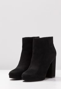 Sorte ruskindsankelstøvler med tykk høj hæl, rund tå og lynlås; glat tekstur og ensfarvet.