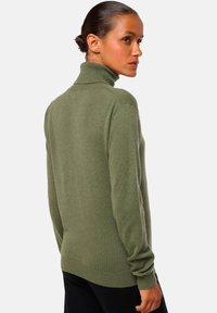 Pull à col roulé vert en tissu tricoté doux, avec des manches longues et une coupe ajustée, doté d'un col et de poignets côtelés.