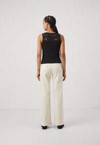 Zwarte mouwloze top met een kanten rugdetail, gecombineerd met witte wijde broekspijpen. De look heeft een aansluitende silhoutte en een gladde textuur.