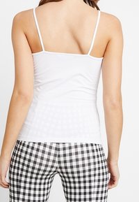 Top in cotone bianco senza maniche con spalline sottili, abbinato a leggings a quadretti bianchi e neri con motivo a scacchi. Texture liscia, design aderente.