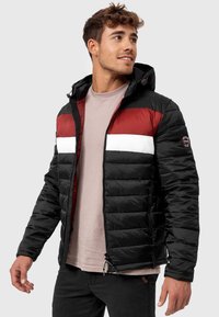Jachetă puffer cu fermoar, neagră și roșie, cu o bandă orizontală albă, având glugă și buzunare cu fermoar. Textură netedă, design matlasat.