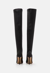 Botas negras hasta la rodilla hechas de tela suave con punta afilada y tacón de aguja. Costuras decorativas en la parte posterior.