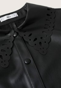 Haut noir en simili cuir avec col festonné comportant des motifs découpés et une fermeture à boutons-pression sur le devant.