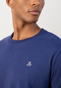 Marineblå bomuld t-shirt med rund hals og korte ærmer, prydet med et lille hvidt broderet "MOP" logo på brystet.