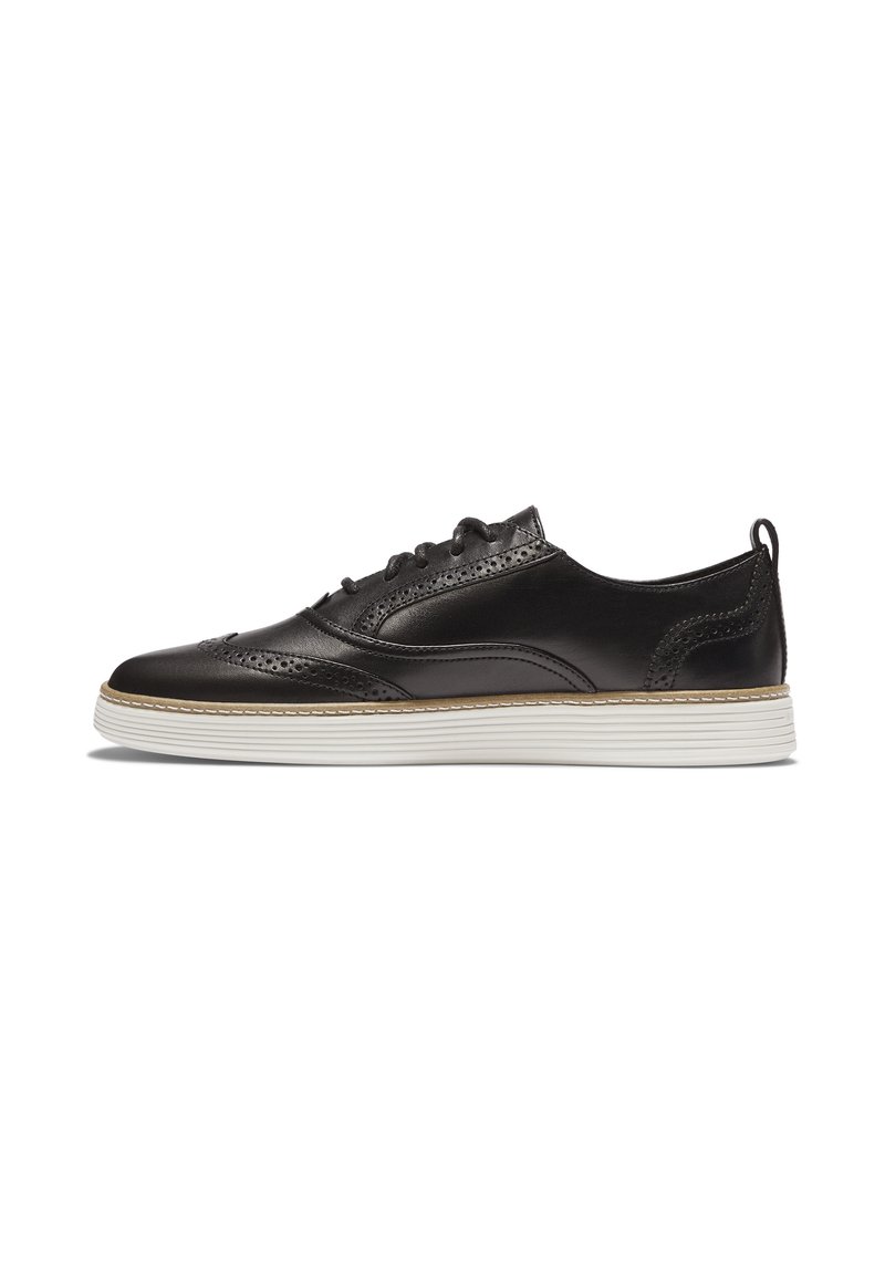 Sneaker in pelle nera con punta a wingtip, suola in gomma bianca e dettagli brogue, visto di lato su uno sfondo bianco.