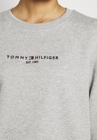 Ljusgrå sweatshirt i bomull med rund halsringning, ribbade muddar och broderad "TOMMY HILFIGER EST. 1985"-logotyp i marinblått och rött.