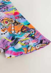 Kirkas, värikäs kangas, jossa on graffitityylisiä kuvituksia ilmapalloista, abstrakteista muodoista ja pinkin, oranssin, sinisen ja keltaisen maalin roiskeista.